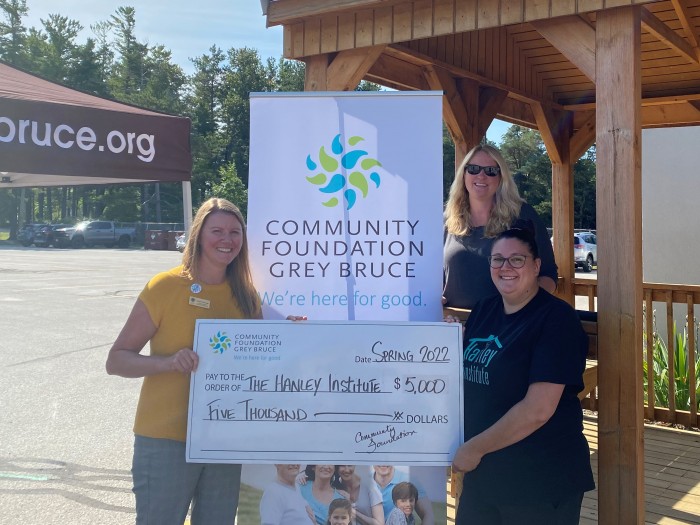 The Hanley Institute holding a large check given to them by Jennifer from The Foundation, in front of the Community Foundation banner