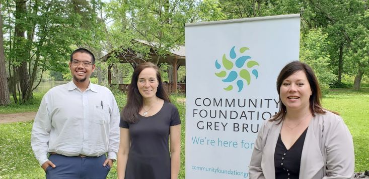 Representing the grantee non-profit organizations are Nicholas Manglag-Ian (Launch Pad), Melri Wright (Ledge Leadership), and Yolanda Ritsema (Big Brothers Big Sisters Kincardine & District) standing in front of the Community Foundation Grey Bruce ba
